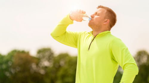 A man wearing a yellow sports shirt keeps hydrated by drinking water from a bottle on a hot sunny day